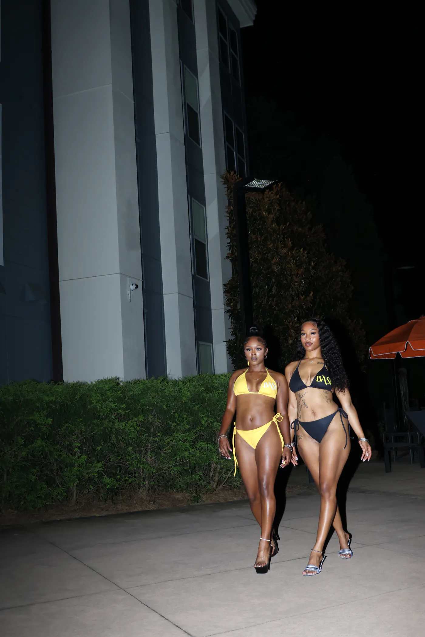 Two models wearing yellow and black Swim BASI string bikinis at night